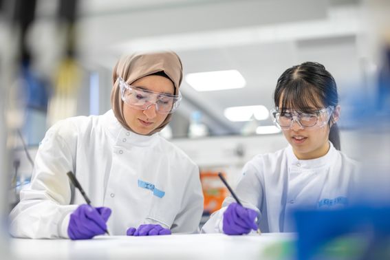 Photo capturing two female medicine scholars in the laboratory environment writing notes