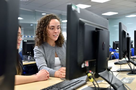 Photo caputuring a smiling woman sat in front of a computer screen with a colleague