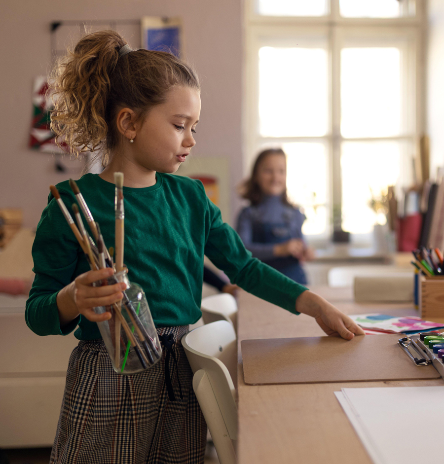 Happy little girl with her friends preparing for art and craft class indoors at school