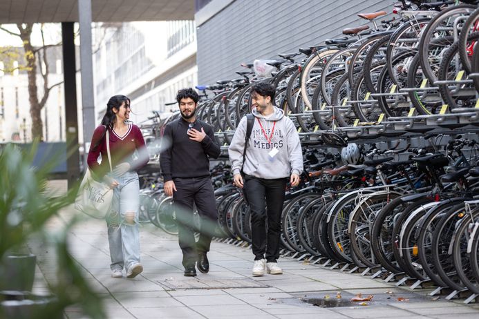 Three students walking past a bike shed