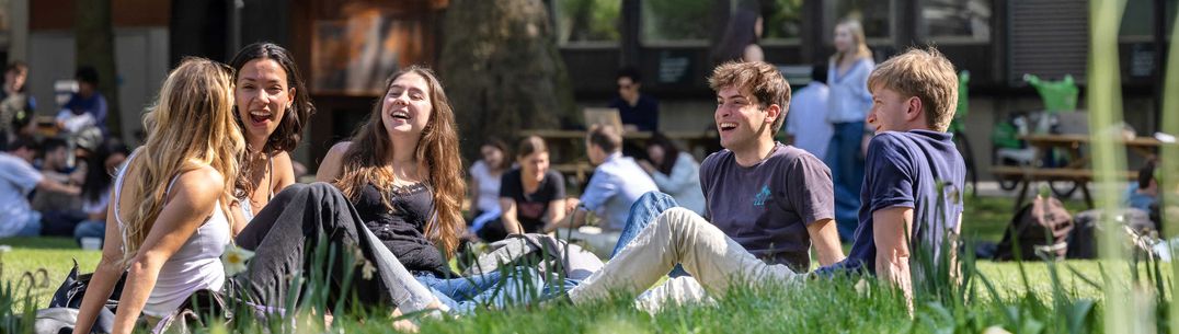 Students sitting on the grass in the spring sunshine at South Kensington campus.