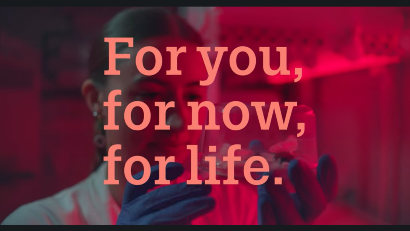 Promotional video thumbnail with the text “For you, for now, for life.” over an image of a person working in a laboratory, with a play button icon.