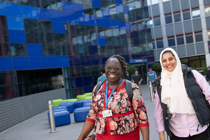 Two staff members walk across Dalby Court, smiling to the camera
